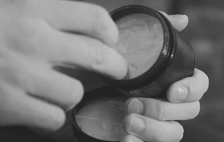 One hand scoops hair pomade out of a small pot