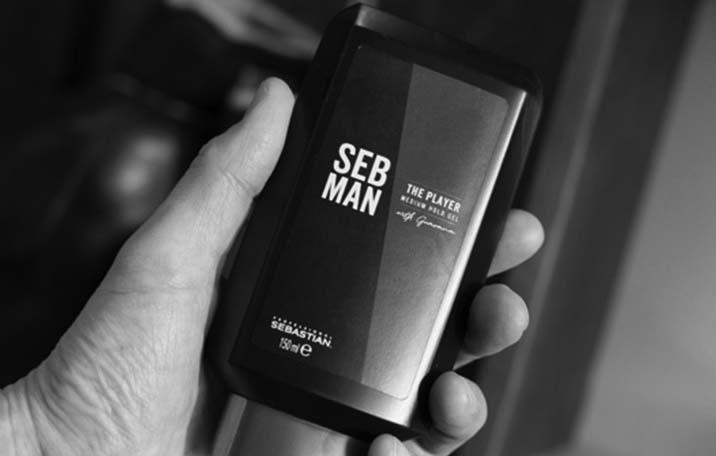 A black bottle of The Player hair styling gel held in a man's hand