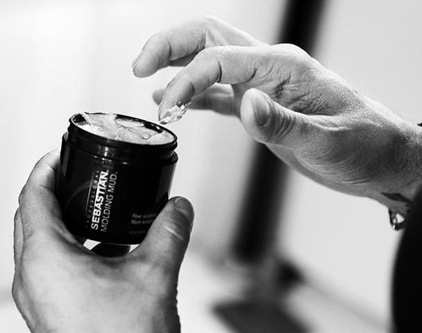 A finger scoops out some Molding Mud hair sculptor from a small black pot